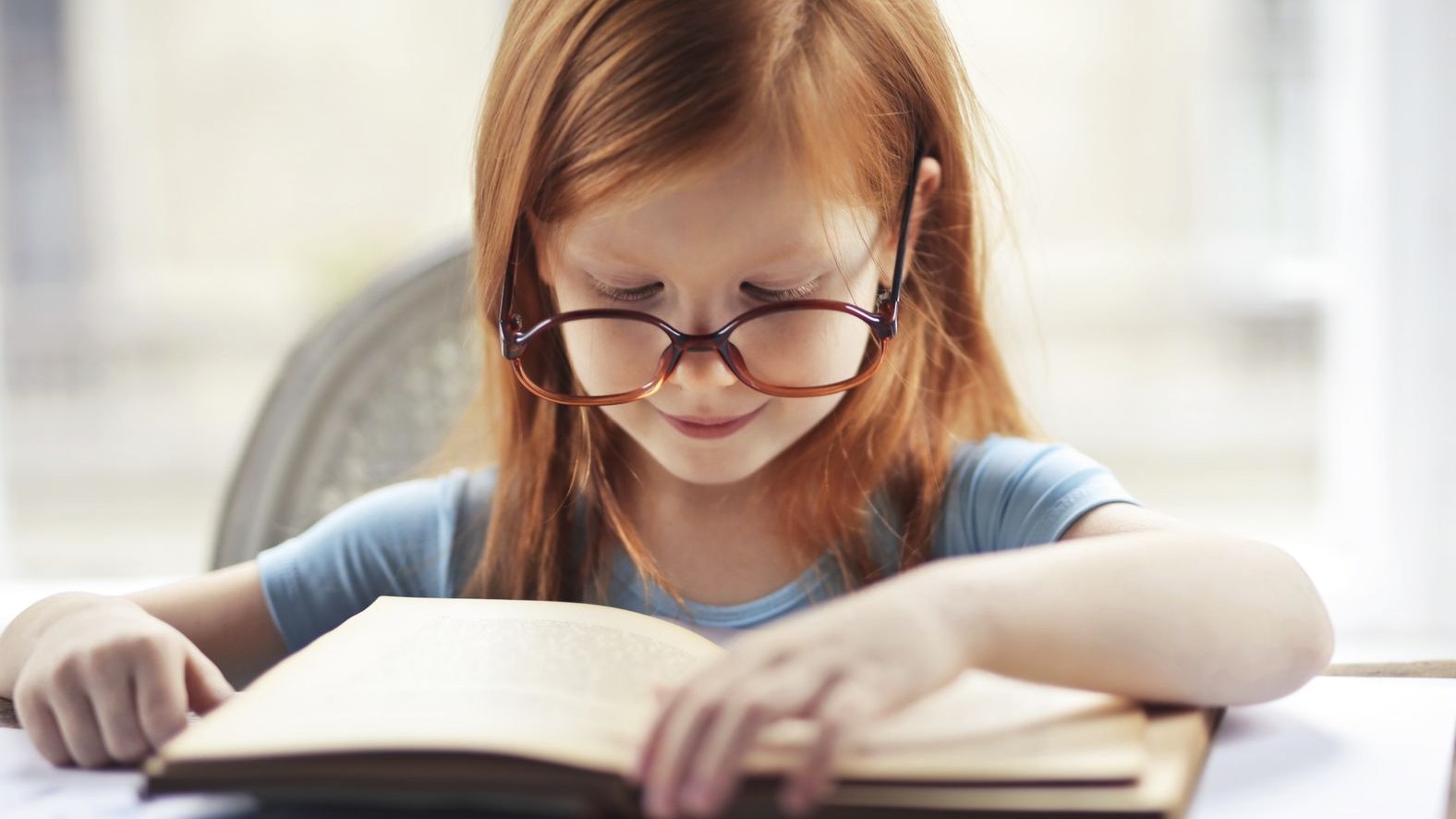 Девочка в очках читает книгу за столом
