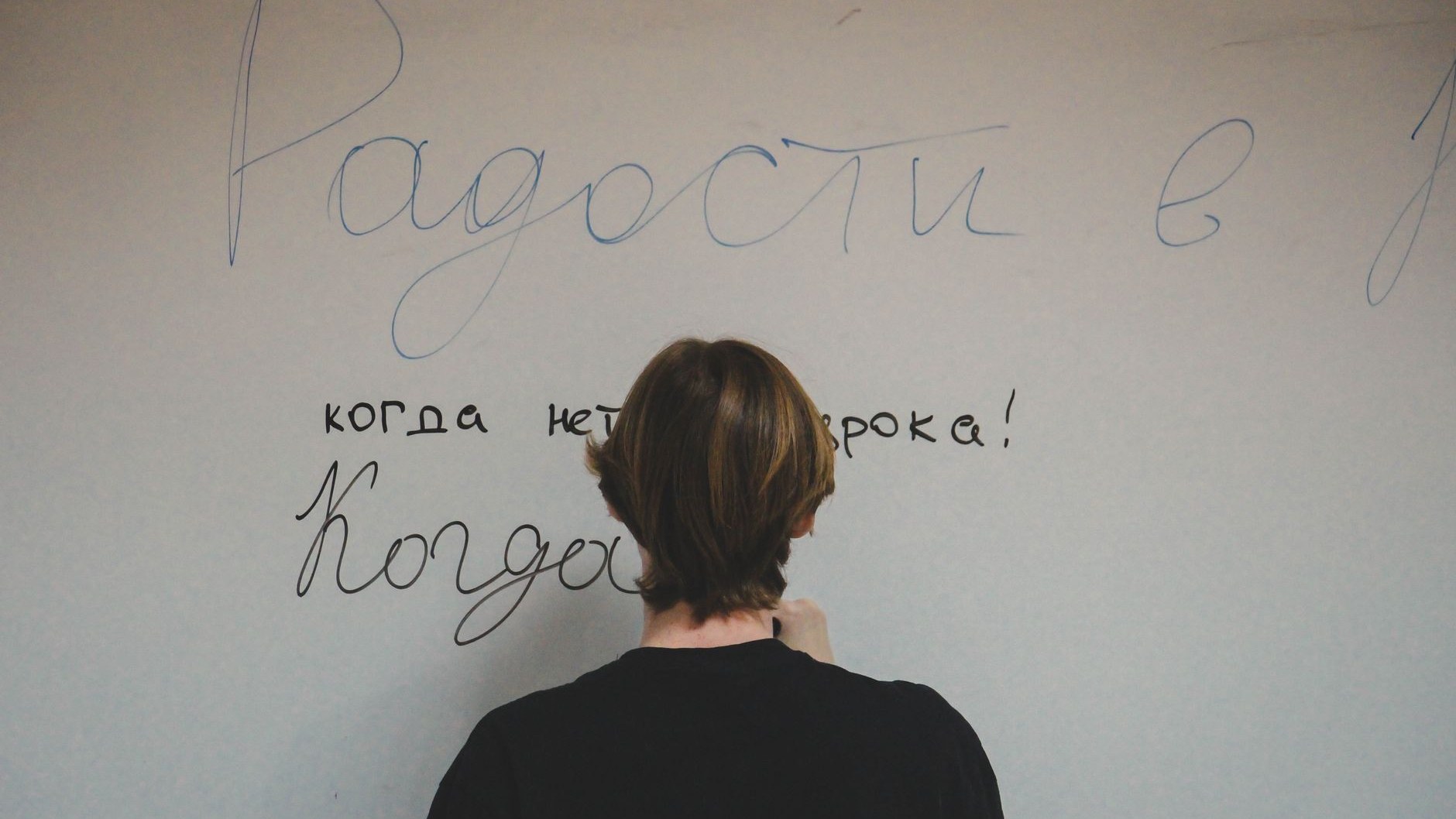 Подросток пишет по-русски на доске, стоя спиной к камере
